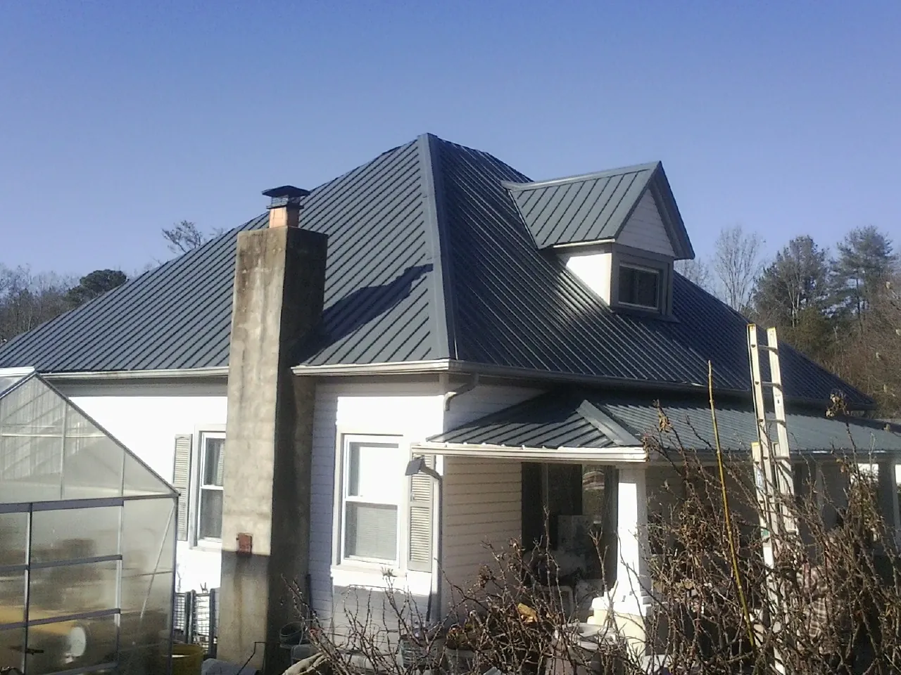 Dark blue standing seam metal roof on a white farmhouse with dormer — Slate & Tile Roof Repair by Roofing Brothers in Chestnut Ridge