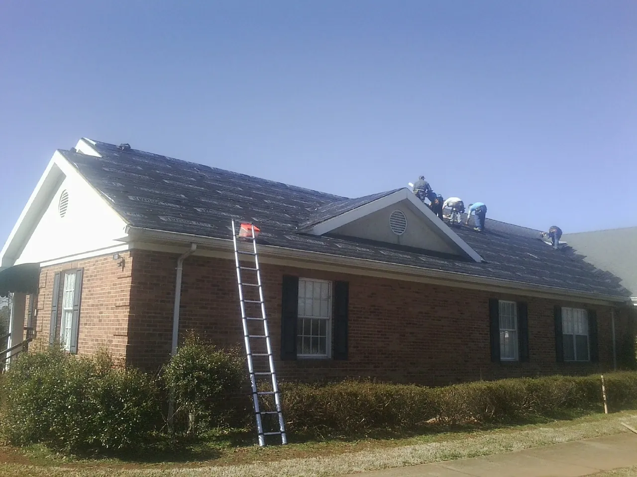 Crew tearing shingles off a brick ranch roof with a ladder set — Metal Roof Repair work by our crew in Chestnut Ridge