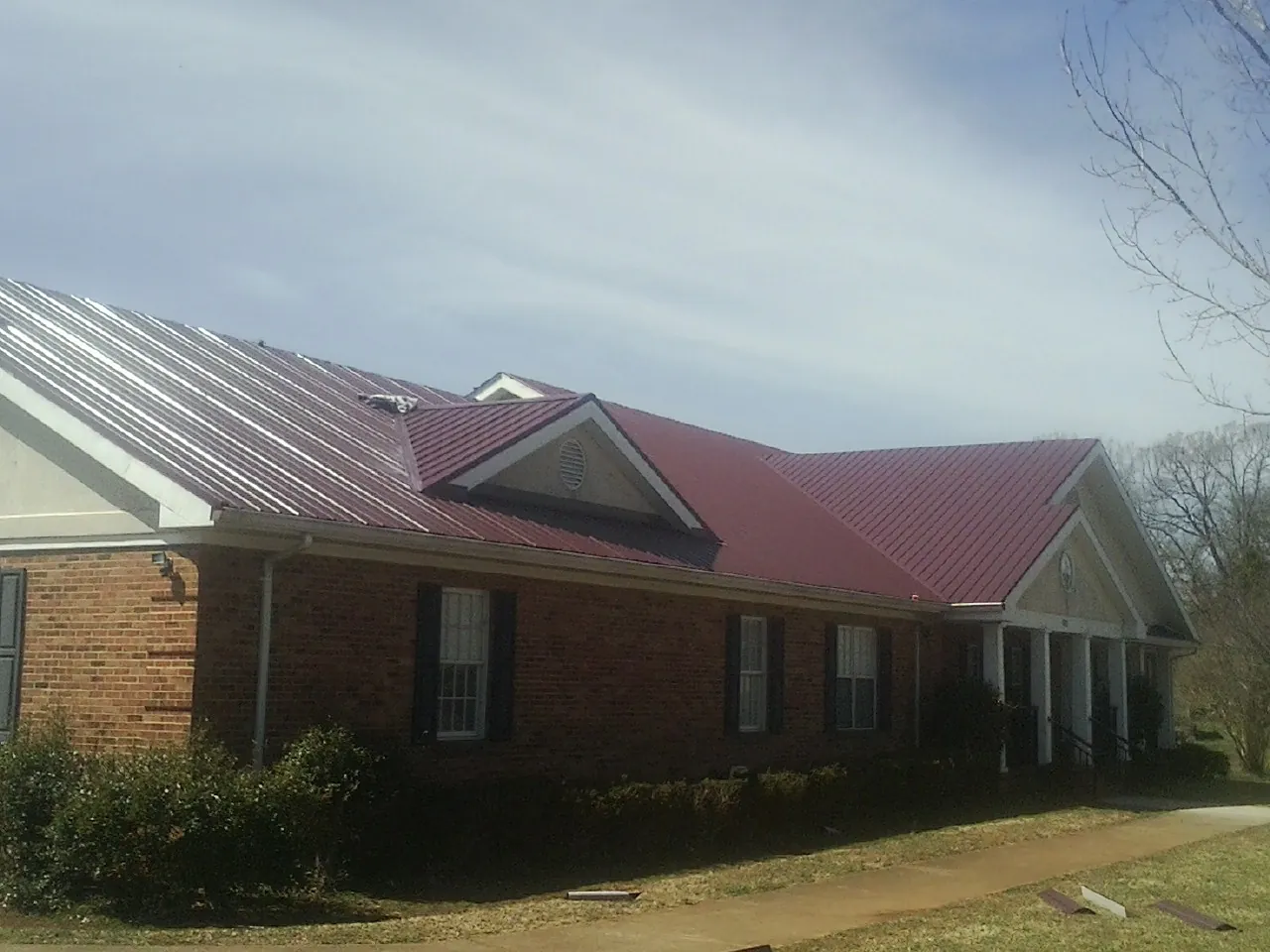 Red metal roof with gabled entries on a long brick building, from a Hail Damage Roof Repair job in Chestnut Ridge