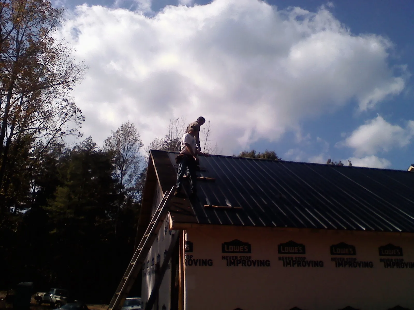 Roofer fastening dark metal panels high against a cloudy sky, from a Roof Inspection job in Chestnut Ridge