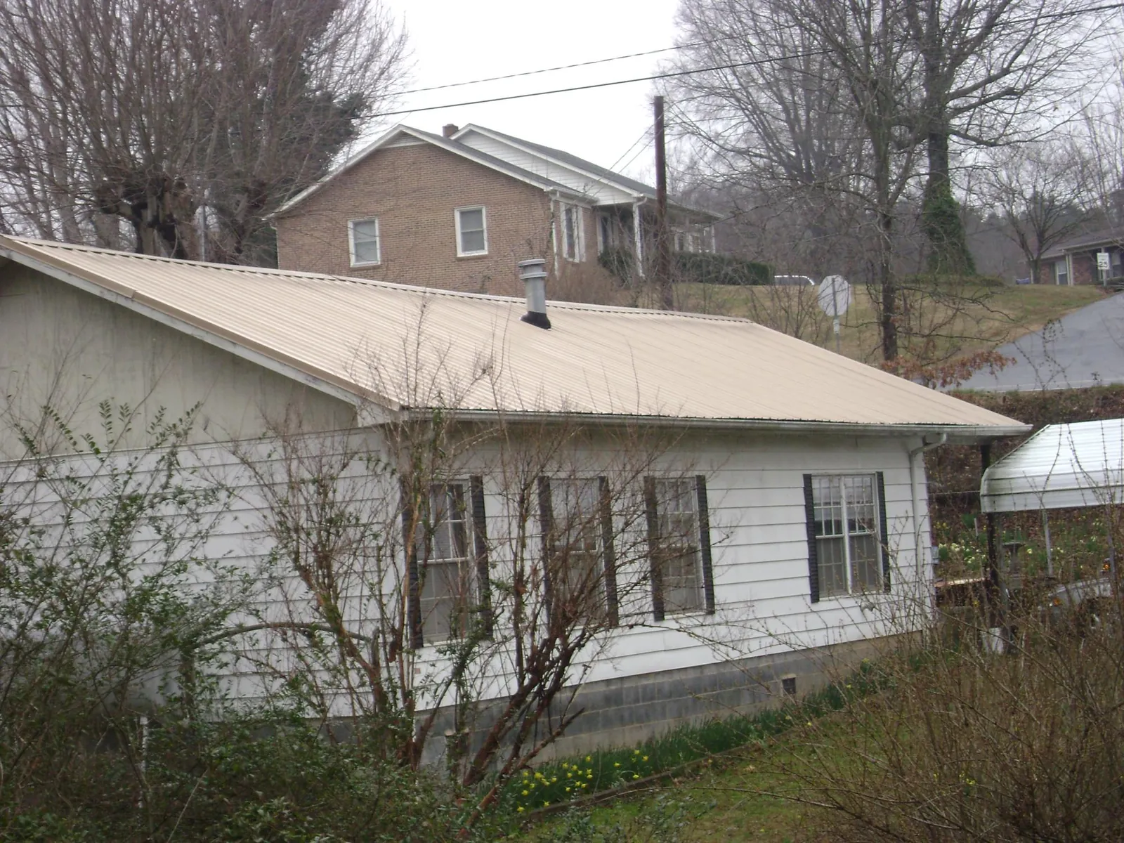 Tan metal roof on a white sided house set into a hillside — Commercial Roofing by Roofing Brothers in Chestnut Ridge