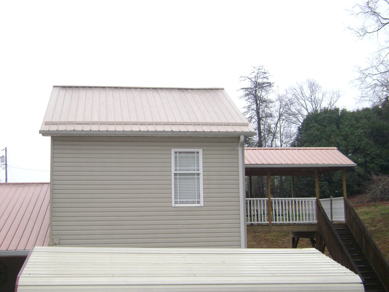 Tan metal roofs on a two story addition and attached porch, from a Roof Replacement job in Chestnut Ridge