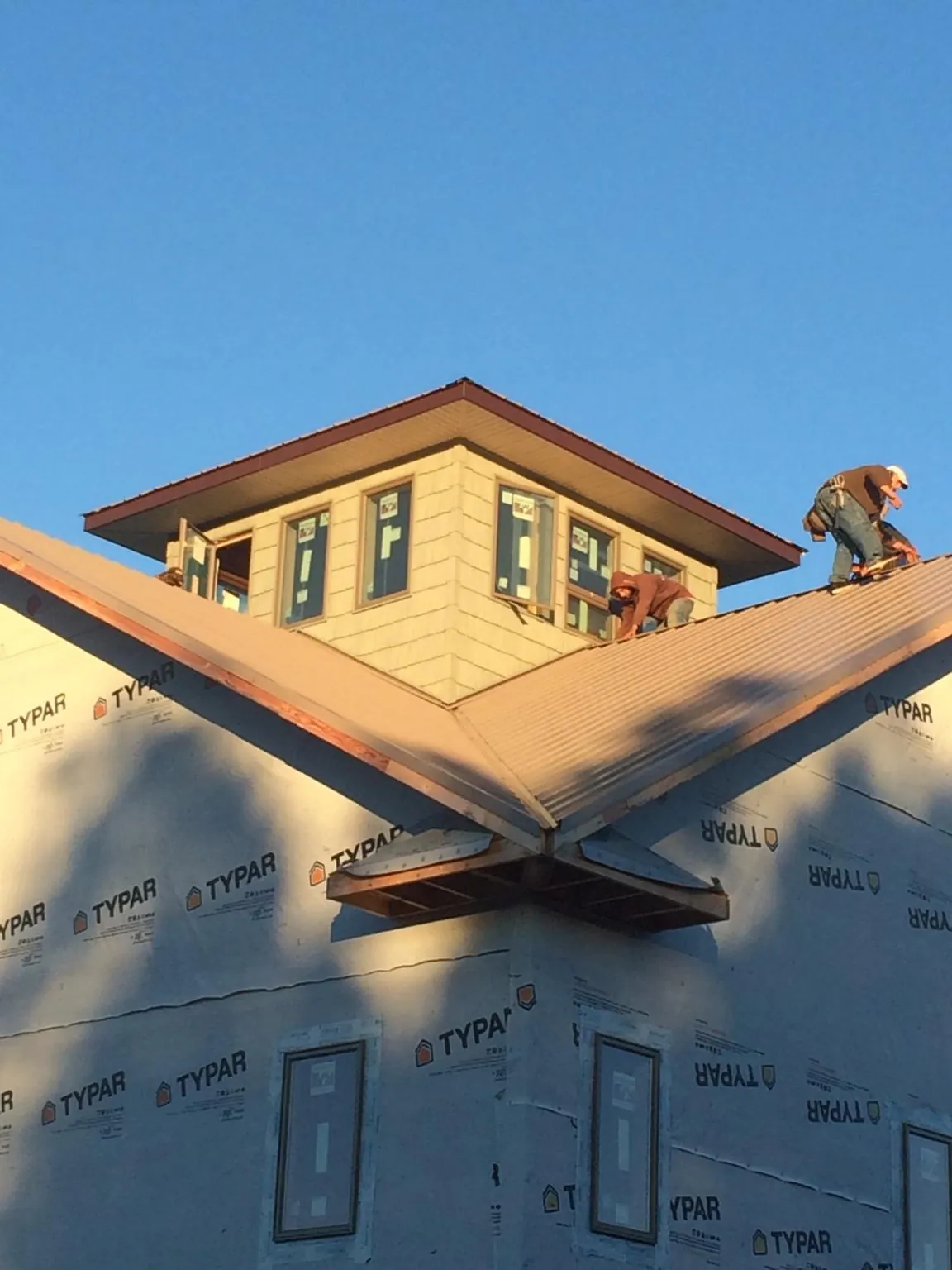 Roofers working around a rooftop cupola on a new metal roof at sunset — Roof Waterproofing in Chestnut Ridge by Roofing Brothers